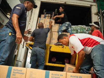 Unos trabajadores descargan cajas de aceite de girasol enriquecido de la parte trasera de un camión, formando una cadena para transportar los alimentos durante una operación de distribución en Venezuela.