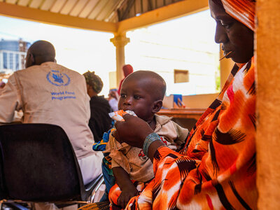 Copilot dijo: Un niño recibe apoyo de nutrición en una clínica del WFP mientras sus cuidadores y los profesionales sanitarios se reúnen durante una sesión comunitaria sobre salud y nutrición.