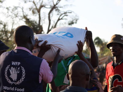 WFP/Nassreen Bachir Un empleado del WFP sostiene un saco de alimentos del WFP junto con otro hombre cuyo rostro está oculto por el saco.