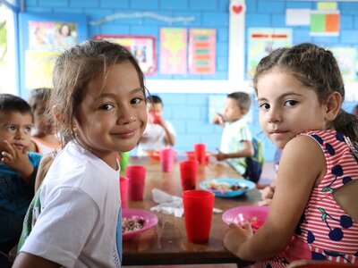Dos niñas en la escuela en la hora de la merienda mirando a cámara.