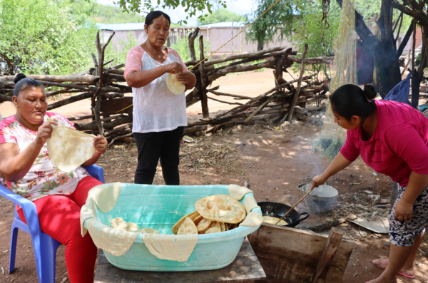 Tres mujeres guaraníes están friendo sopaipillaen un fogón al aire libre. La sopaipilla es masa de harina estirada que se sirve como bastimento en las comidas guaraníes. , una 