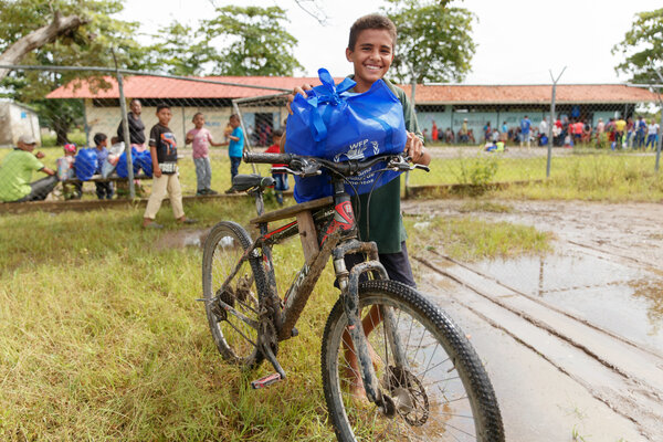 Un niño se acerca en una bicicleta con una ración de alimentos que acaba de recibir en su escuela.