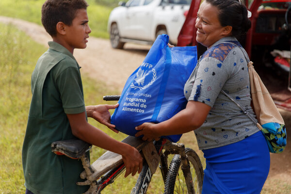 Un niño en bicicleta entrega una ración de alimentos a una mujer.
