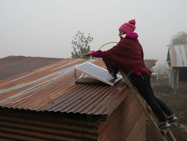 Una mujer instala un panel solar en el techo de una casa de zinc en medio de la niebla en la Sierra de los Cuchumatanes. 