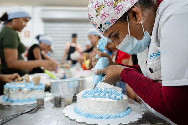 Una mujer decora una torta en una reposteria. 