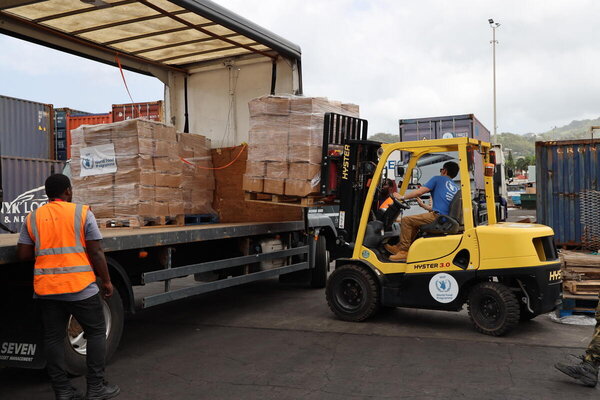 Descarga de alimentos llegados desde Barbados en el puerto de San Vicente y las Granadinas. Un montacargas amarillo descarga los alimentos encajetados desde un camión.