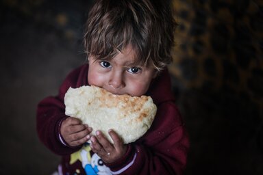 Abboud eating a loaf of freshly baked bread that this mom baked in their clay oven with the wheat flour they receive from WFP