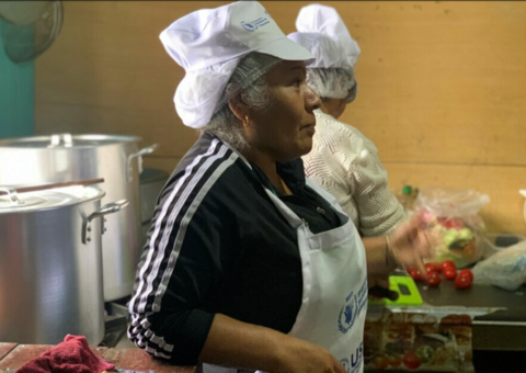 Señora peruana con un delantal de WFP y su malla para el cabello trabajando en la cocina