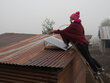 Una mujer rural instala un panel solar en el techo de una casa hecha con hojas de zinc en la Sierra de los Cuchumatanes, Guatemala.