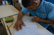 A man in blue shirt sits at a school desk writing out numbers