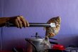  Una mano sostiene un pez frito con unas pinzas de cocina sobre una estufa. Al fondo se observan una olla metálica y recipientes plásticos rojos, con una pared morada como fondo. Foto: WFP / Colombia