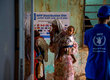A woman holds a baby in front of a WFP sign