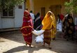 Dos mujeres sudanesas llevan un saco de alimentos color blanco. Las mujeres visten la ropa tradicional de color morado y amarillo. Foto: WFP/ Bubakar Garelnabei
