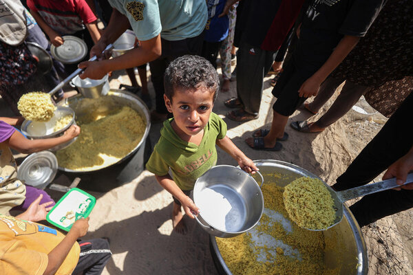 WFP/Ali Jadallah. In the photo, kids are receiving and eating rice which they brought from a nearby WFP-supported hot meals kitchen. Kids would wait for hours patiently for this meal. They usually took the food back to the family's tent. Gaza, Palestine.