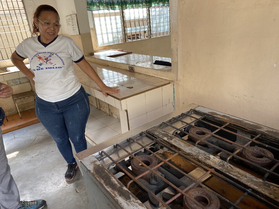 Una mujer está de pie al lado de la estufa oxidada en la cocina de una escuela en Venezuela.  