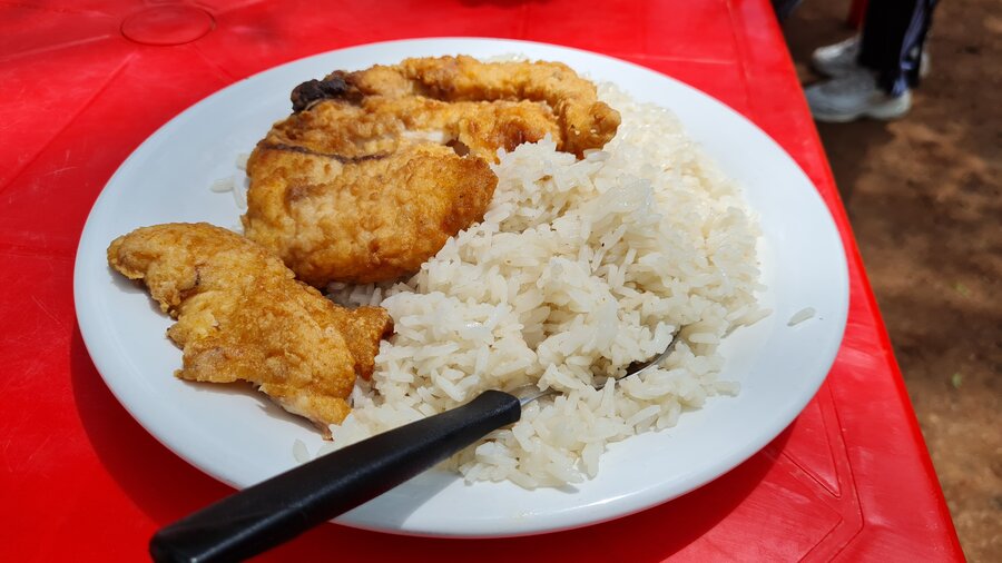 Un plato de arroz con surubí frito es servido en una mesa con mantel rojo. En el plato hay un tenedor.