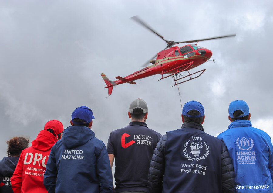 Un helicóptero rojo se eleva mientras seis personas lo observan.