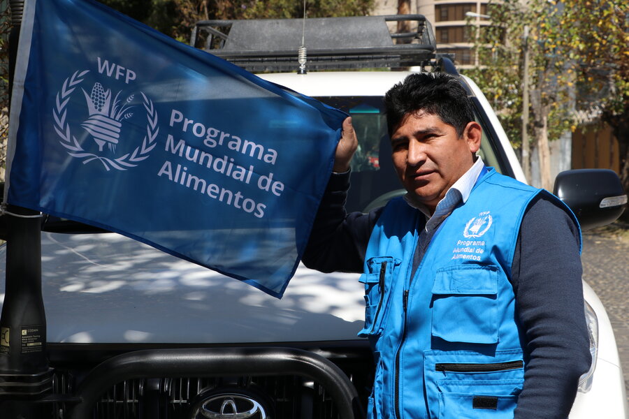 Wilder Mamani sostiene la bandera del Programa Mundial de Alimentos frente a su vehículo.