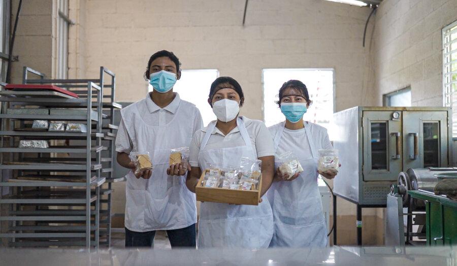 Tres panaderos salvadoreños muestran sus productos en la cocina.