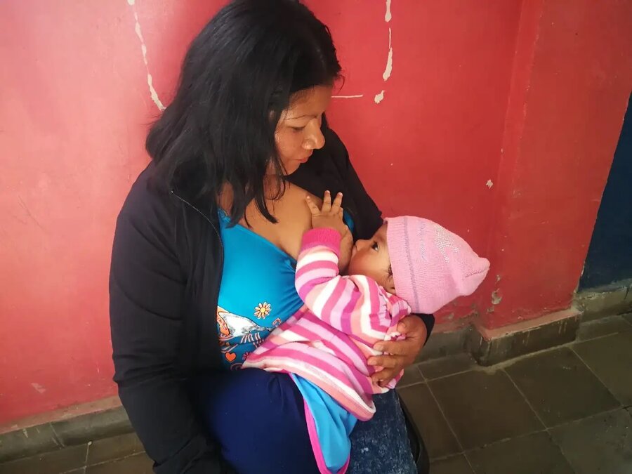 Una mujer amamanta a su bebé mientras espera recibir asistencia alimentaria del Programa Mundial de Alimentos.