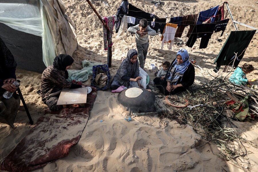 Three Palestinian women sit on the floor with children making bread in a camp for displaced people