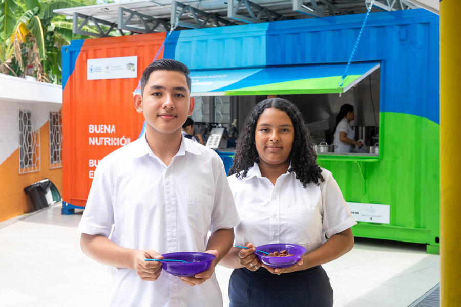 Dos estudiantes sosteniendo platos de comida frente a KIAB