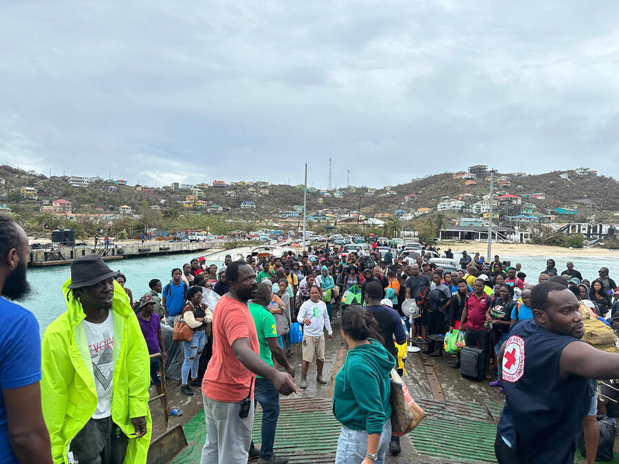 Una multitud de residentes de la Isla Unión se preparan para abordar el ferry y abandonar la isla tras el paso del huracán Beryl. Al fondo pueden verse las casas destrozadas por el huracán.