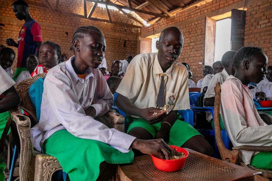 Students wearing white shirts and green shorts and skirts tuck into a WFP-provided school meal in South Sudan. Photo: WFP/Eulalia Berlanga