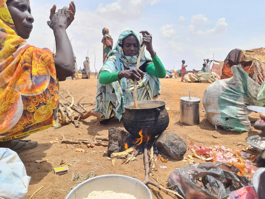 Sudanese women gathered around a fire cooking a pot of food at a dusty displacement camp. Photo: WFP/Mohmamed Galal