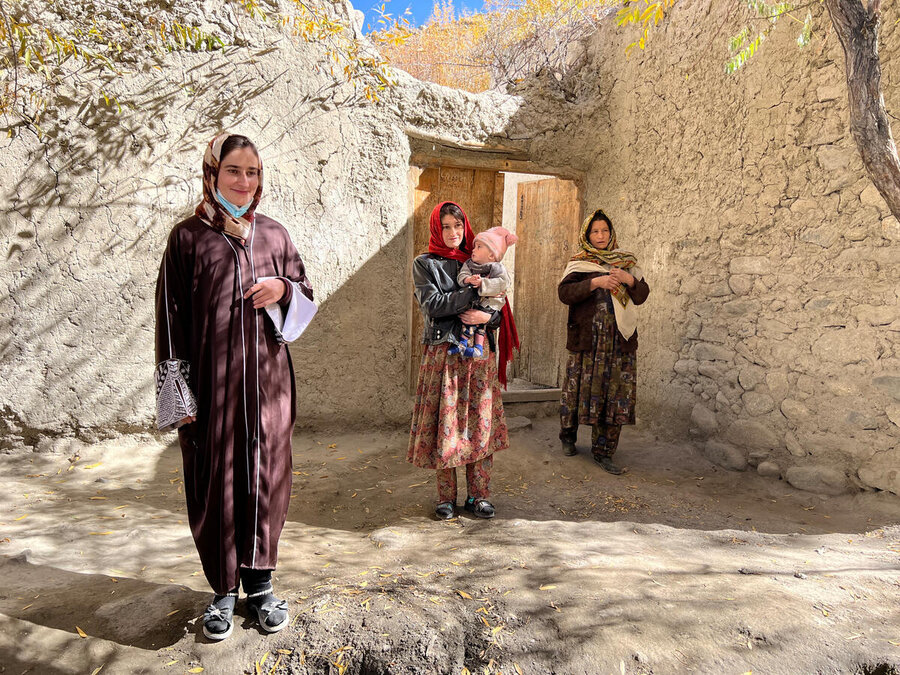Three women in colourful gowns standing in the sunlight in front of a stone dwelling, with two cradling babies. Photo: WFP/Isheeta Sumra 