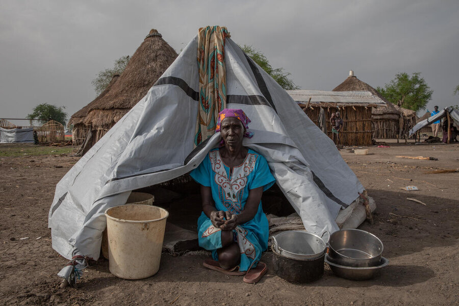 A woman sits in front of a makeshift tent in a dirt field, with thatched huts in the background. Photo: WFP/Gabriela Vivacqua