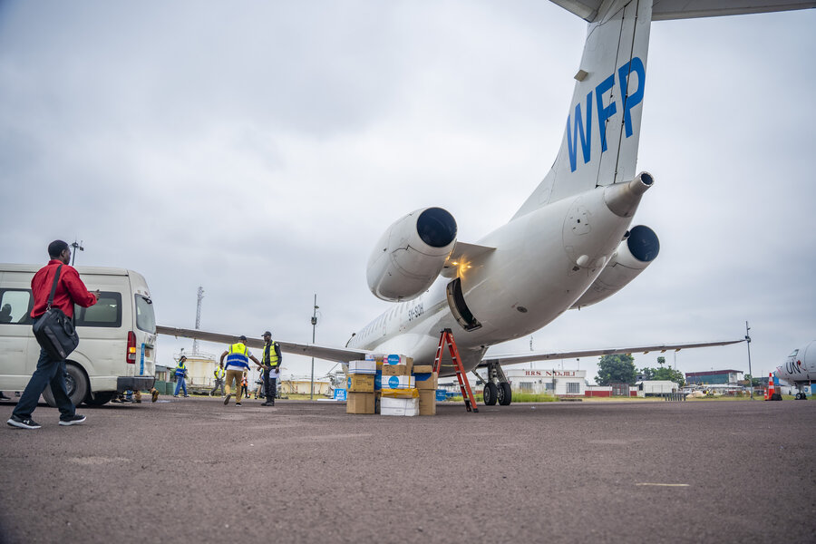 A person heads to a white plane with a WFP logo on it, with boxes piled upon the tarmac waiting to be loaded. Photo: WFP/Michael Castofas