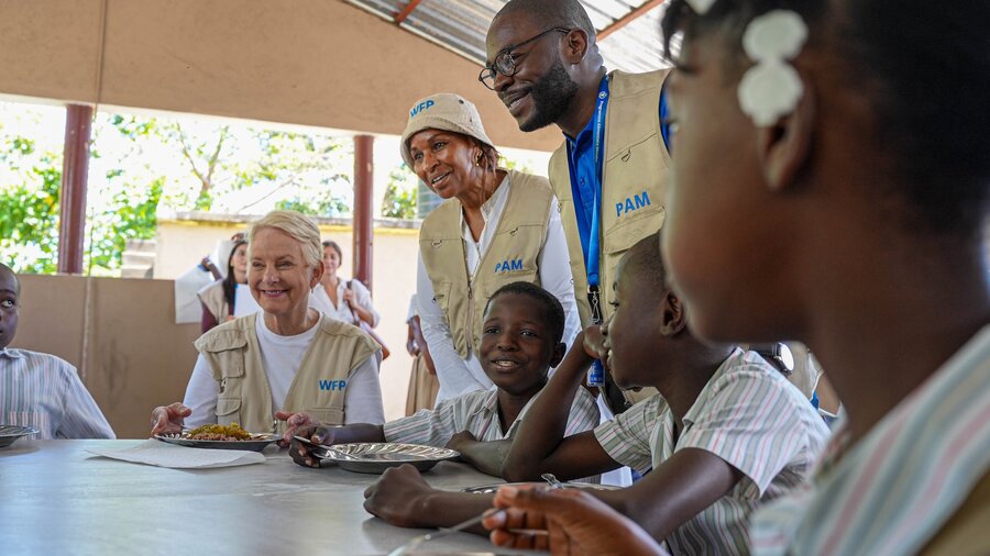 WFP staff in tan vests sit around a table outside speaking to young schoolchildren. Photo: WFP/Pedro Rodrigues