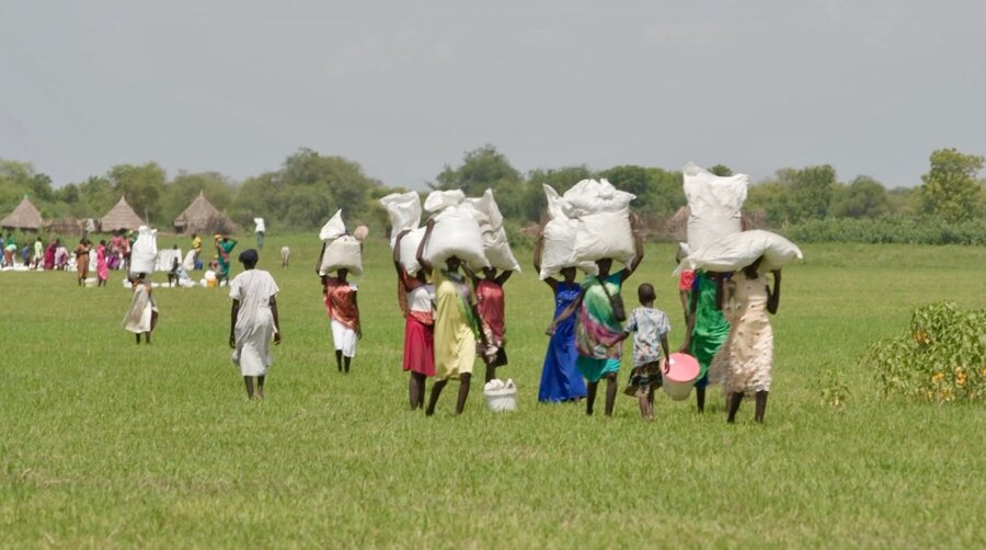 People walk through a large grassy field carrying large white sacks on their head. Photo: WFP/Gabriela Vivacqua