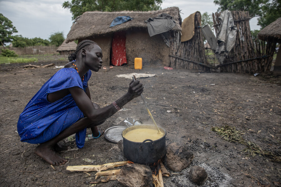 A woman cooks a pot over an open fire, backdropped by a mud house with a straw roof. Photo: WFP/Gabriela Vivacqua