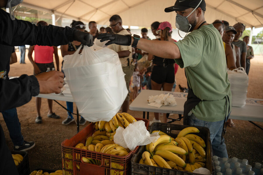A man stands in a large hall handing out containers of food. Photo: WFP/Gustavo Vera