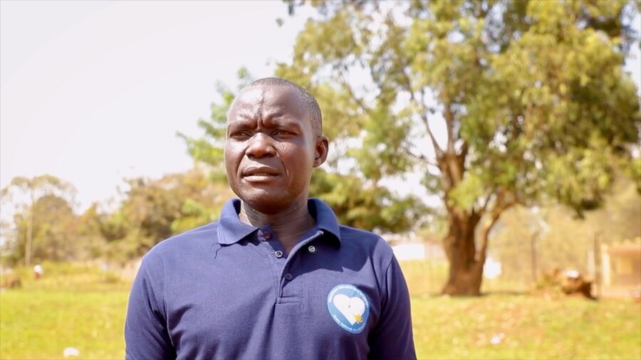A man with a blue shirt with a heart on it stands in front of a grassy plain. Photo: WFP/Arete/Seros Muyisa