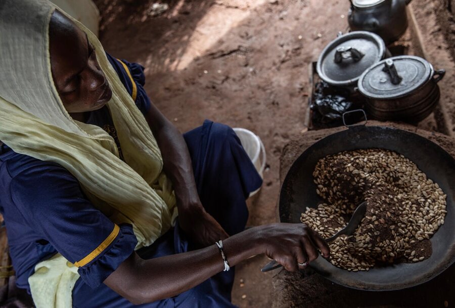 A woman in a yellow headscarf and blue gown cooks grains over an open fire. Photo: WFP/Gabriela Vivacqua