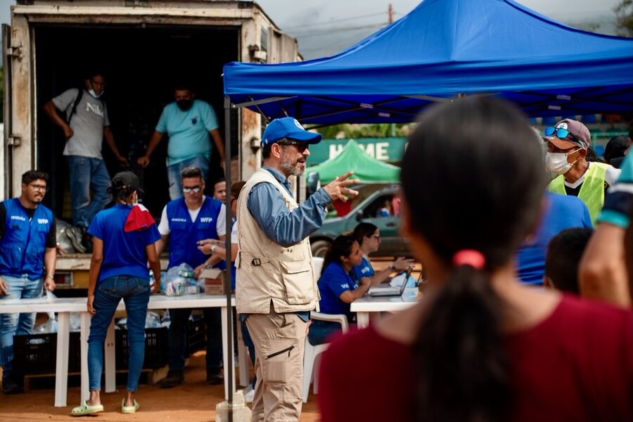 A man in a WFP T-shirt speaks to a crowd of people with other WFP staff in the background. Photo: WFP/Gustavo Vera