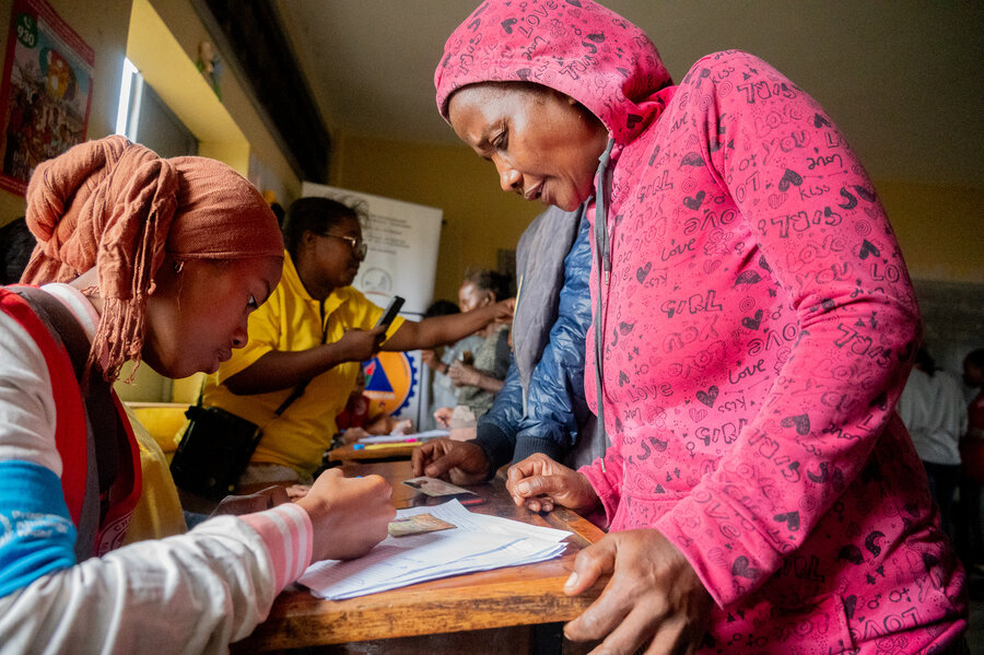 A woman in a pink hooded jacket stands in front of desk getting checked off to receive WFP assistance. Photo: WFP/Jerry Andrianaivoarivony 