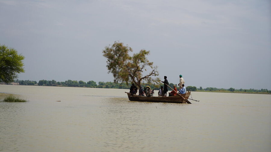 Men navigate a wooden boat through floodwaters in Pakistan. Photo: Dinar Ahmad