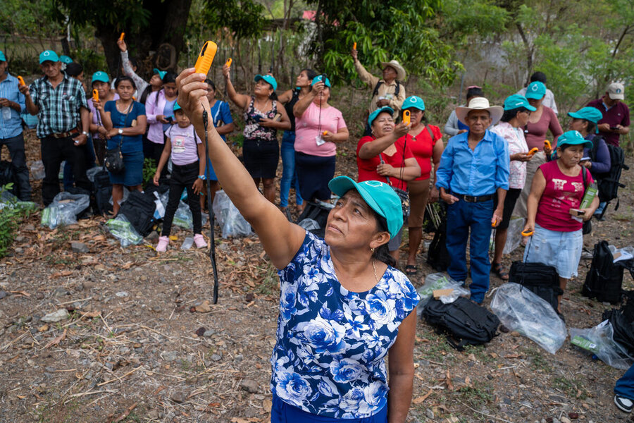 People participate in a field training session, holding handheld devices aloft while gathered outdoors in a rural area.
