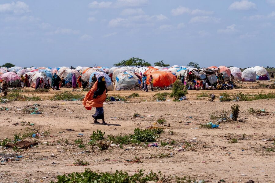 A woman in a long dress through sandy land backdropped by a sea of tents. Photo: WFP/Sara Cuevas Gallardo