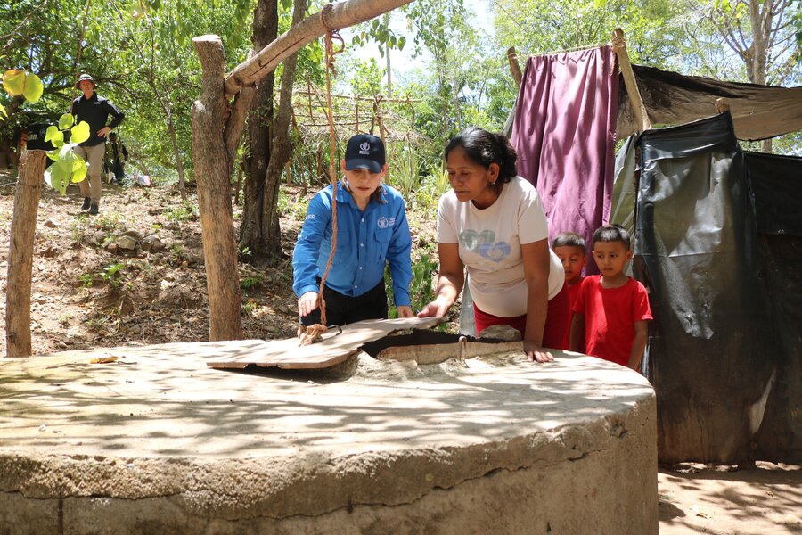 A woman wearing a blue WFP cap and long-sleeve shirt stands next to another woman and her children surveilling a well. Photo: WFP/Darlan Bautista