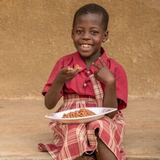 Niña sonriendo con uniforme escolar mientras come arroz en un plato blanco