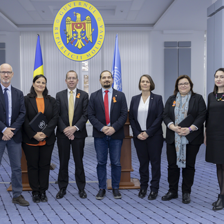 Un grupo de siete personas en fila, delante del emblema y las banderas del gobierno moldavo. Visten de manera formal.