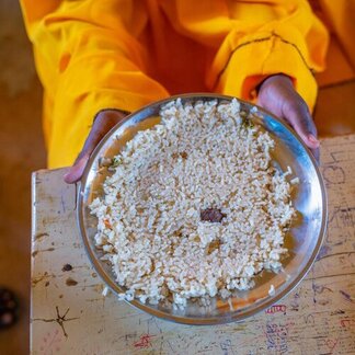 Un niño sostiene un plato metálico con una pequeña ración de arroz, lo que muestra la escasa comida disponible en el entorno escolar.