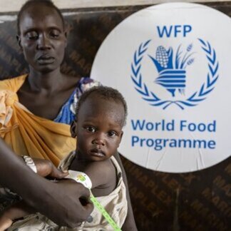 Trabajador del Programa Mundial de Alimentos mide el brazo de un niño en brazos de su madre, frente a un cartel del WFP