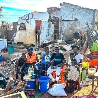 Personas sentadas frente a casas destruidas por el ciclón Chido.